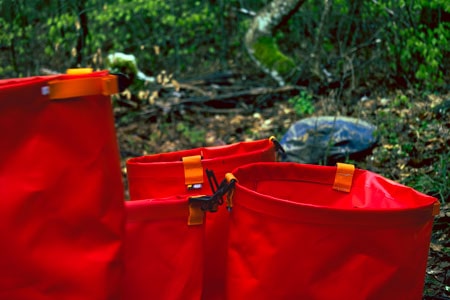 Drei rote ergonomische Pflanztaschen stehen im Wald, bereit für die Herbstpflanzung von Setzlingen.